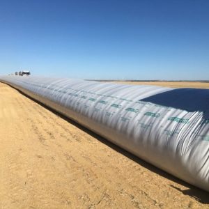 Farm field with a large Grain Bagging storage bag under clear sky.